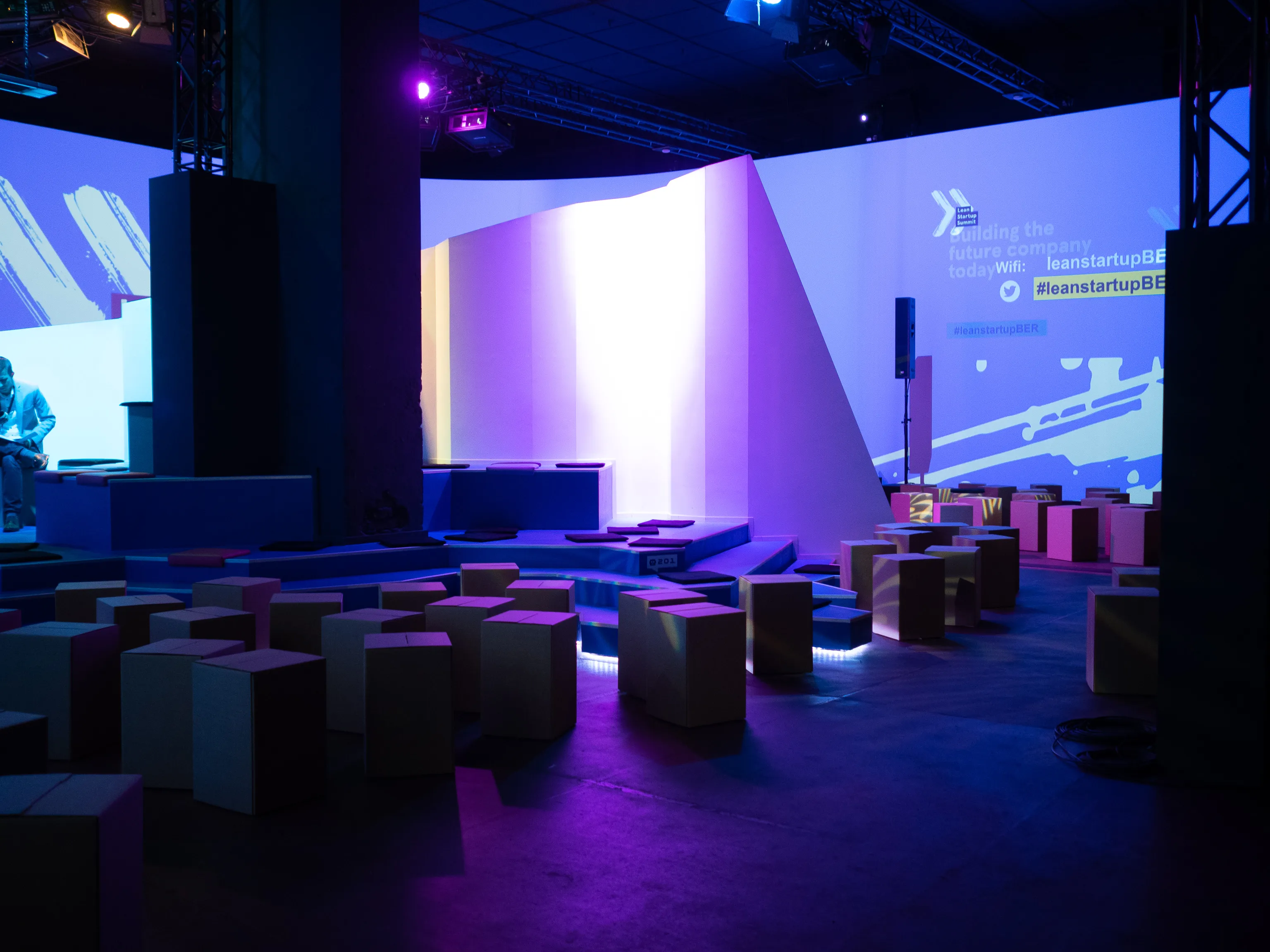 An empty blue-and-purple event space with cube seating and projected branding.