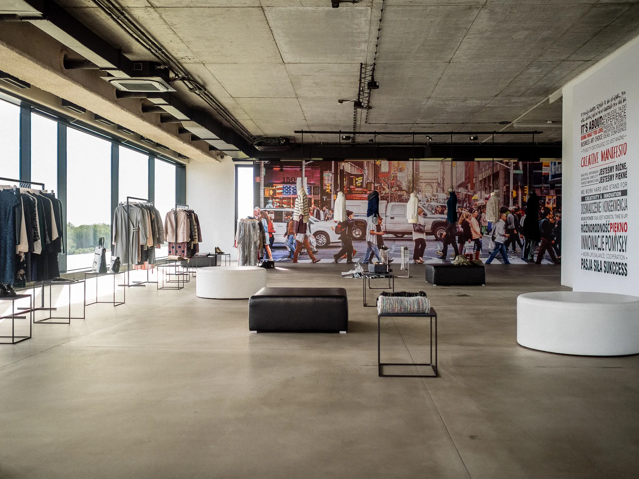 Wide view of the Quiosque showroom with clothing displays, seating, and a city mural.