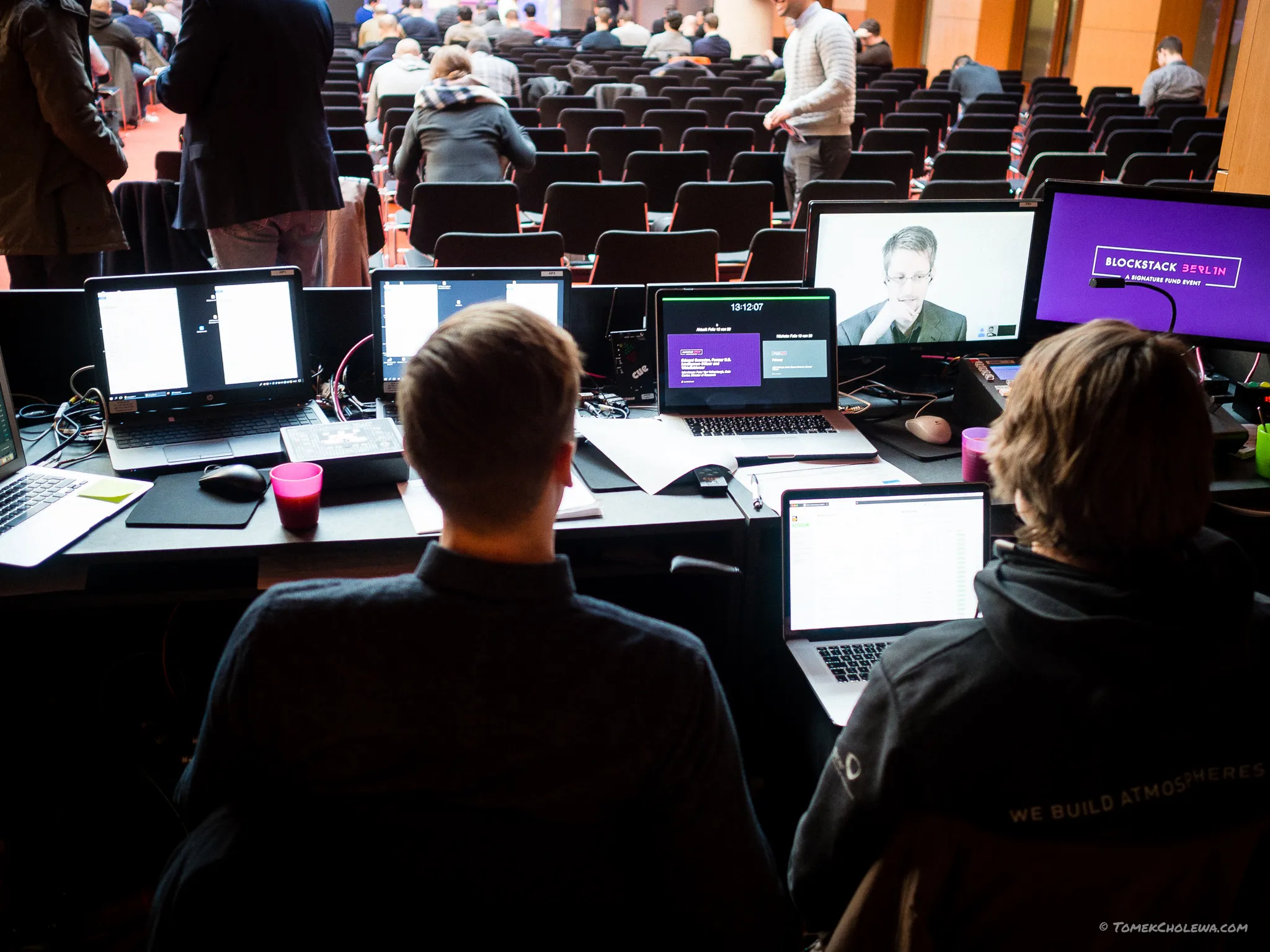 Event technicians work at a laptop-filled control desk behind the auditorium.
