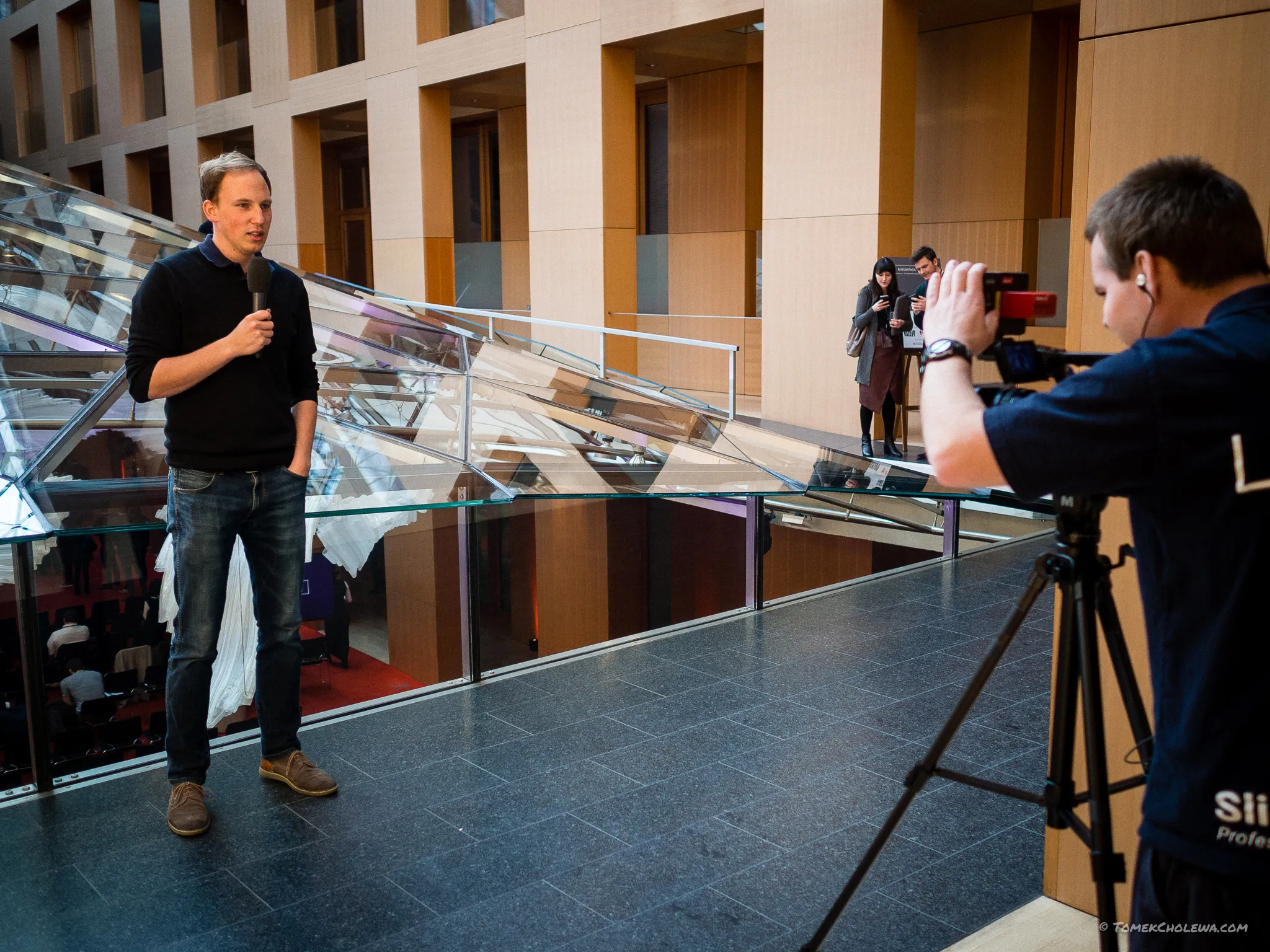 A camera operator films an attendee speaking into a microphone in the atrium.