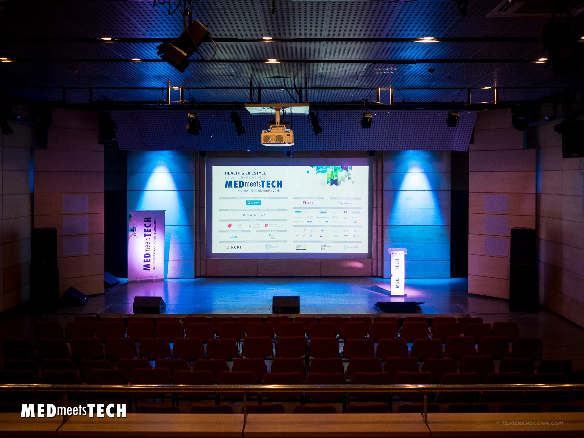 An empty blue-lit Med Meets Tech stage faces rows of red auditorium seats.