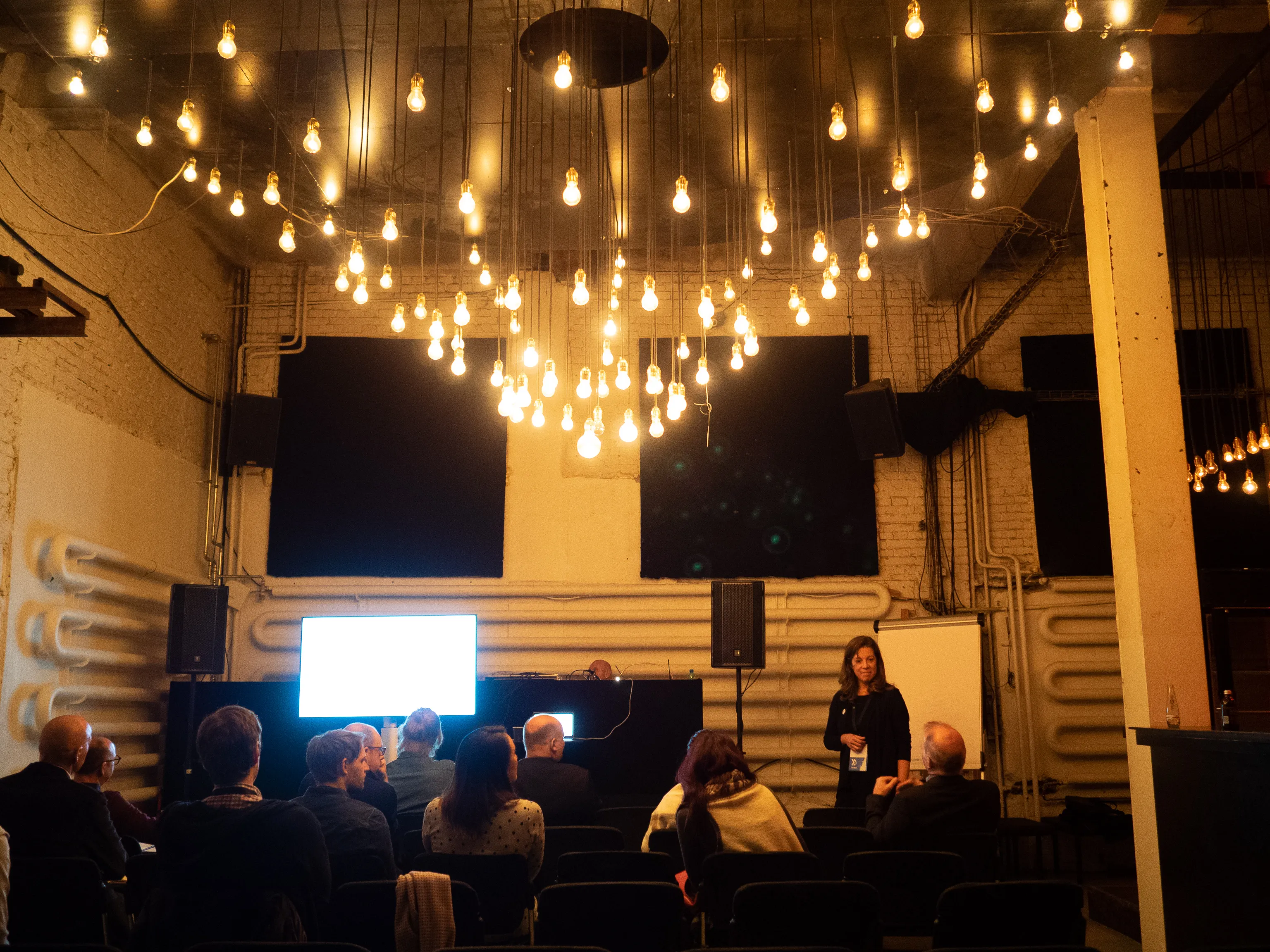 A woman leads a breakout session beneath a canopy of hanging bulbs.