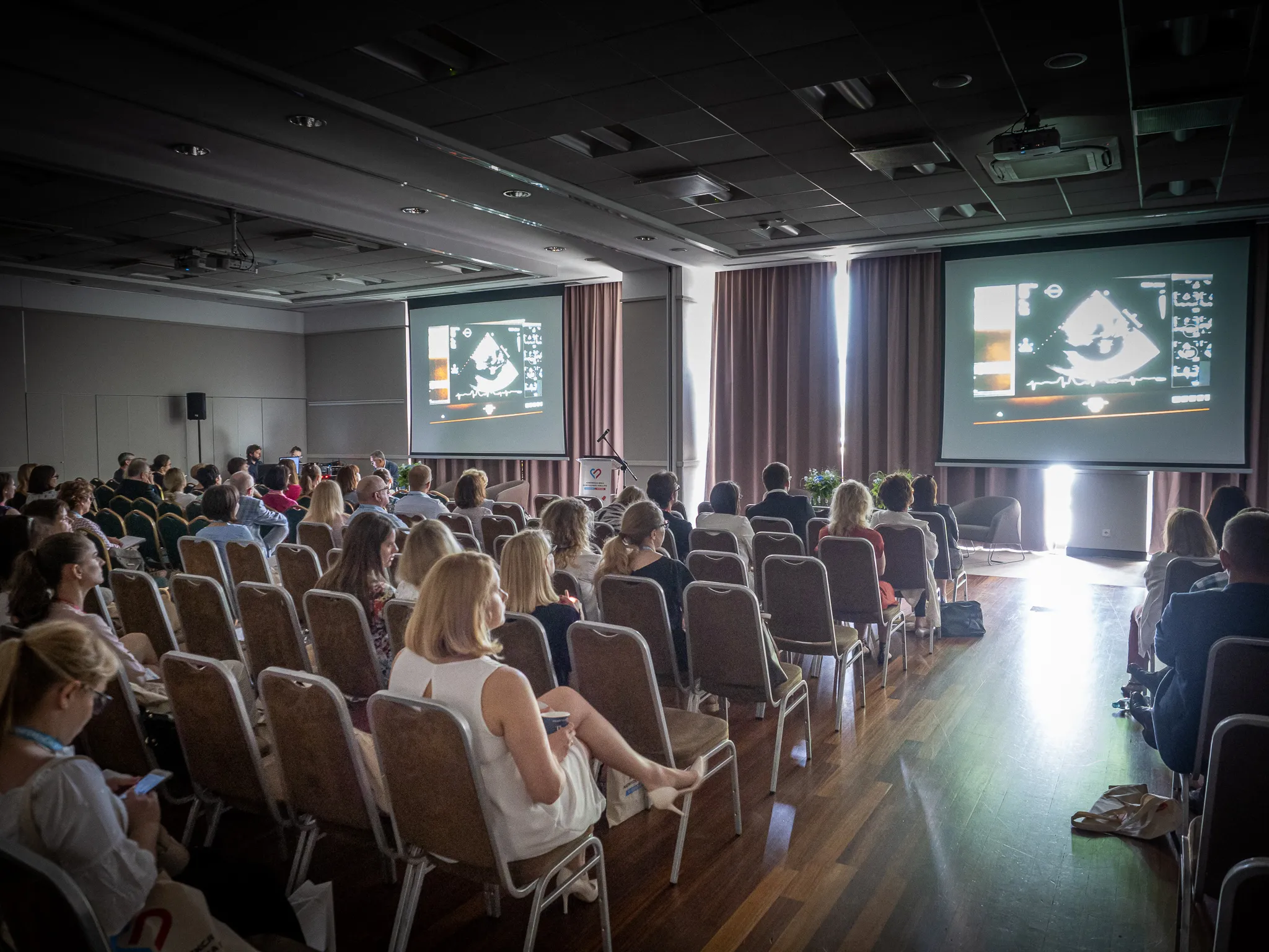 A medical conference audience watches diagnostic images projected on two screens.