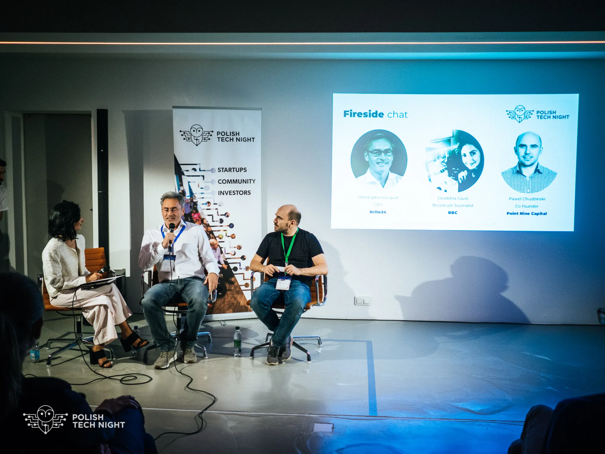 A moderator and two guests take part in a fireside chat onstage.