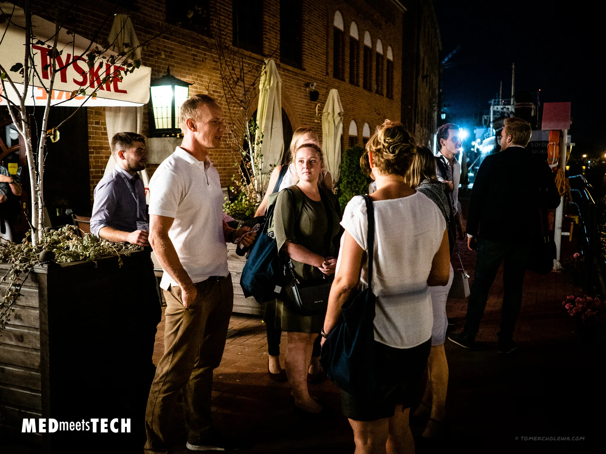 Groups of attendees network on a brick-lined terrace at night.