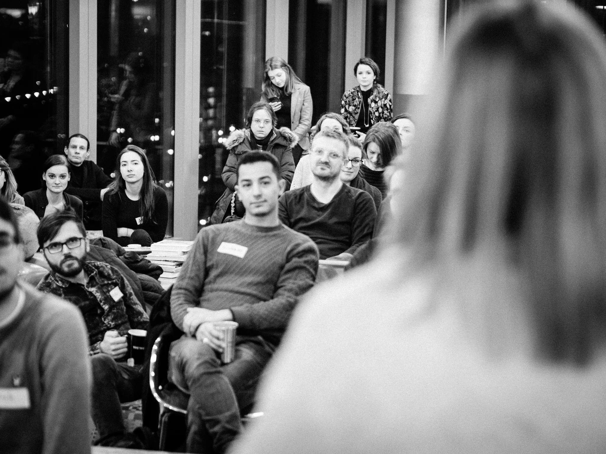 A seated audience listens to a speaker in a black-and-white event photograph.