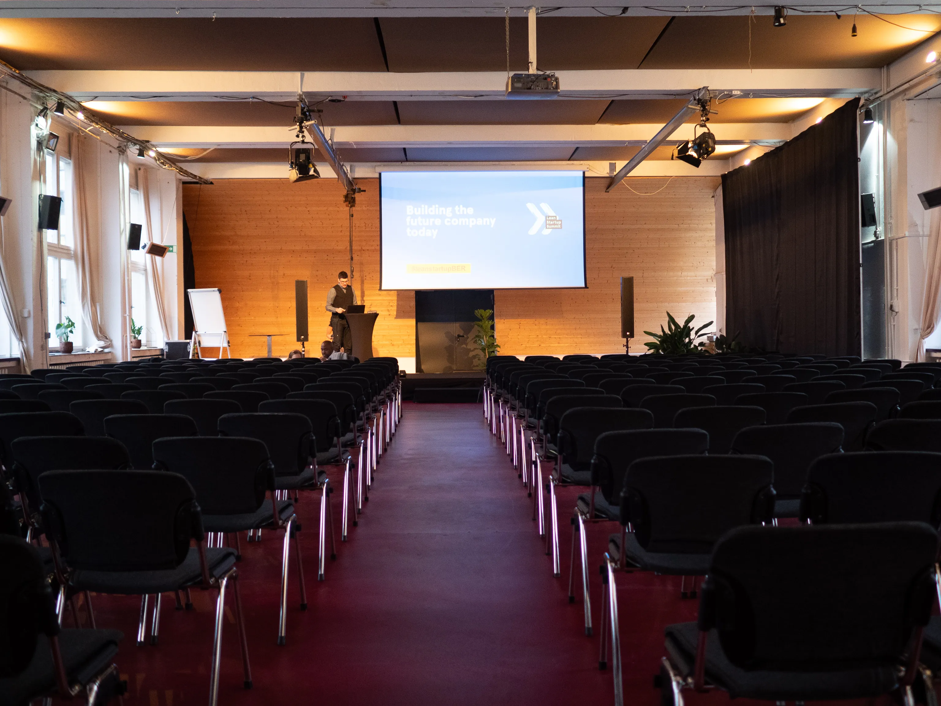 A presenter prepares onstage in a nearly empty lecture hall.