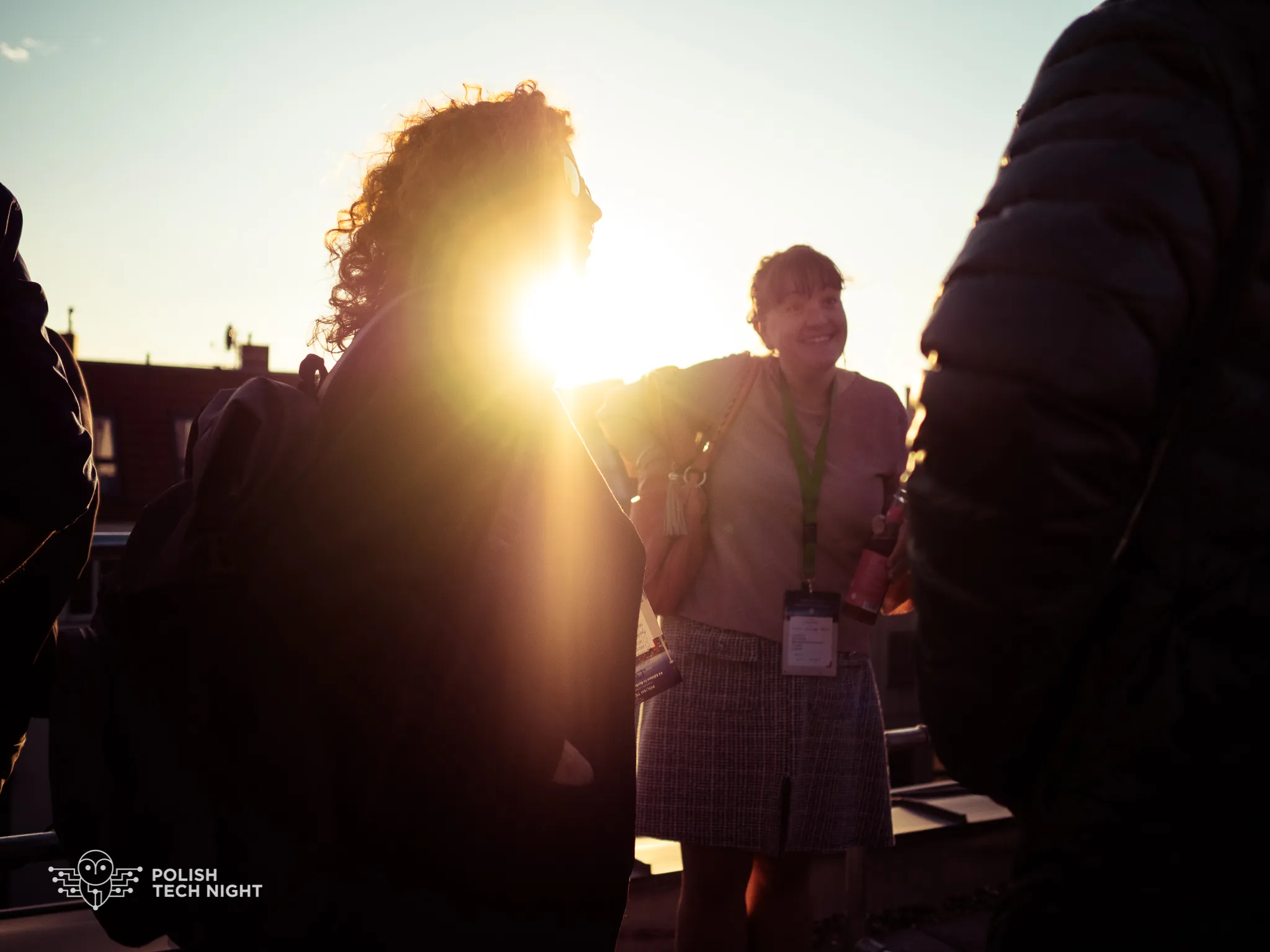 Rooftop attendees talk in strong sunset backlight.