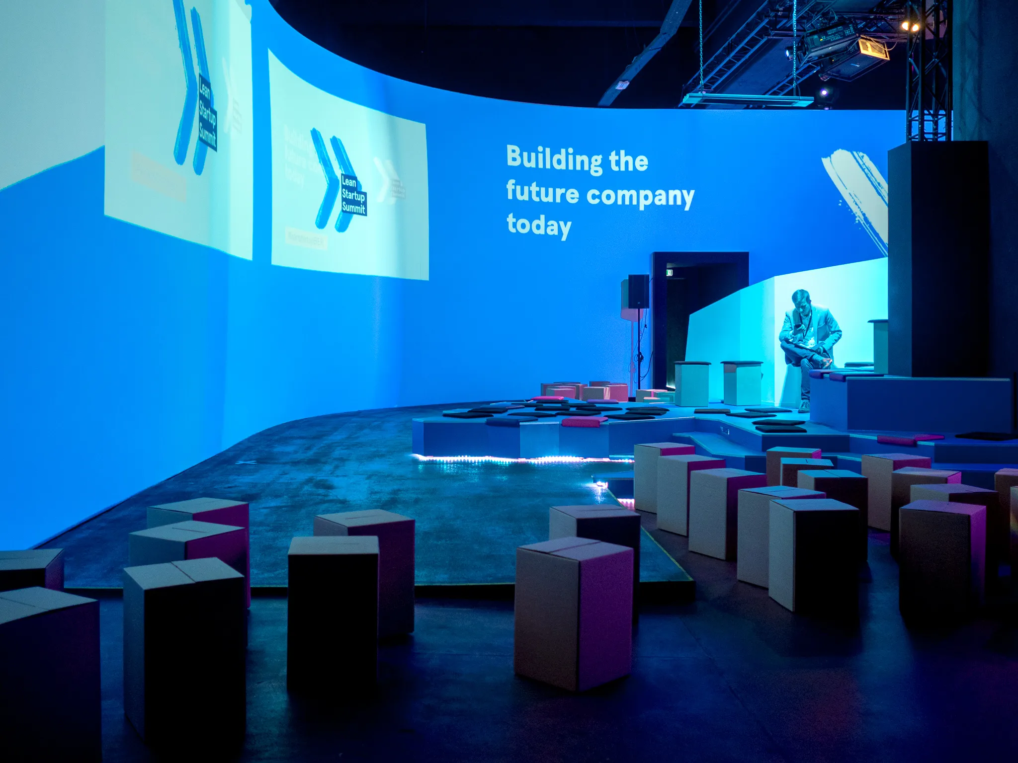 A lone person sits among cube seats on the blue-lit main stage.